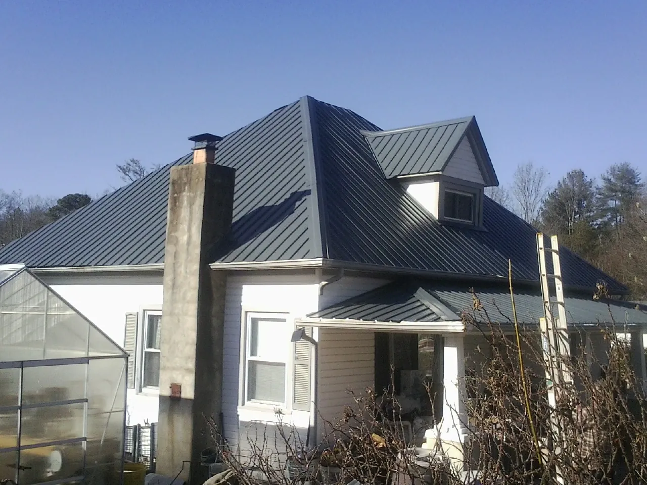 Dark blue standing seam metal roof on a white farmhouse with dormer — Slate & Tile Roof Repair by Roofing Brothers in Langston