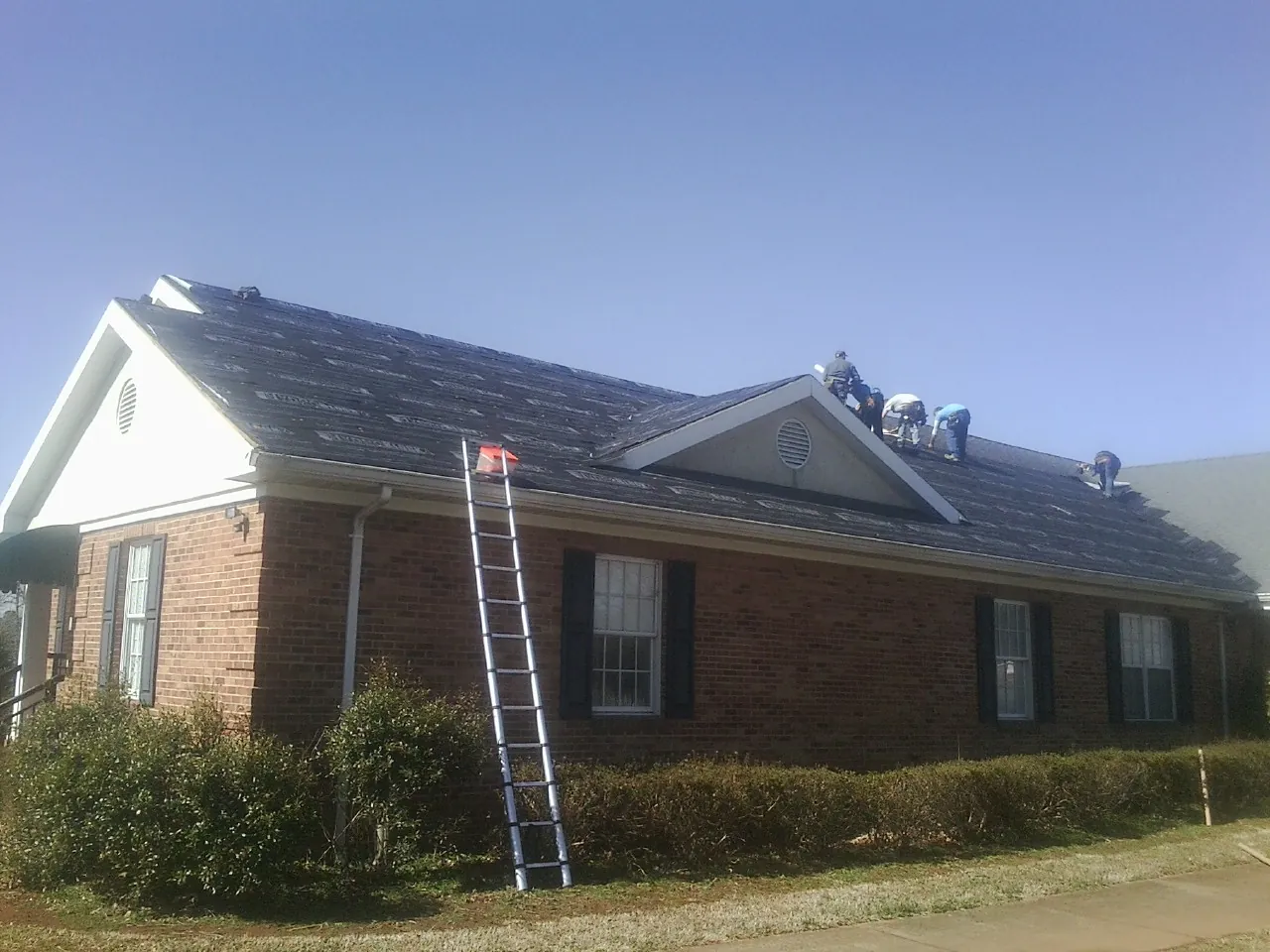 Crew tearing shingles off a brick ranch roof with a ladder set — Emergency Roof Repair work by our crew in Langston