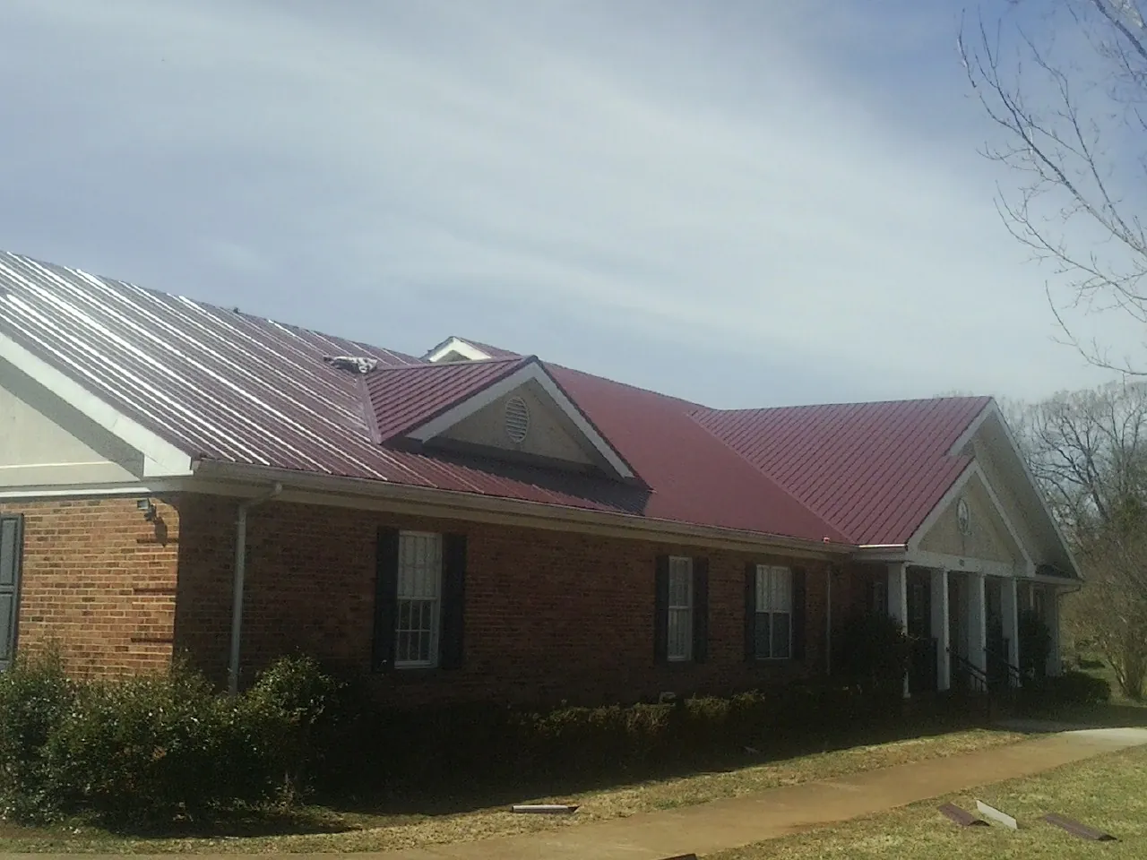 Red metal roof with gabled entries on a long brick building, from a Hail Damage Roof Repair job in Langston