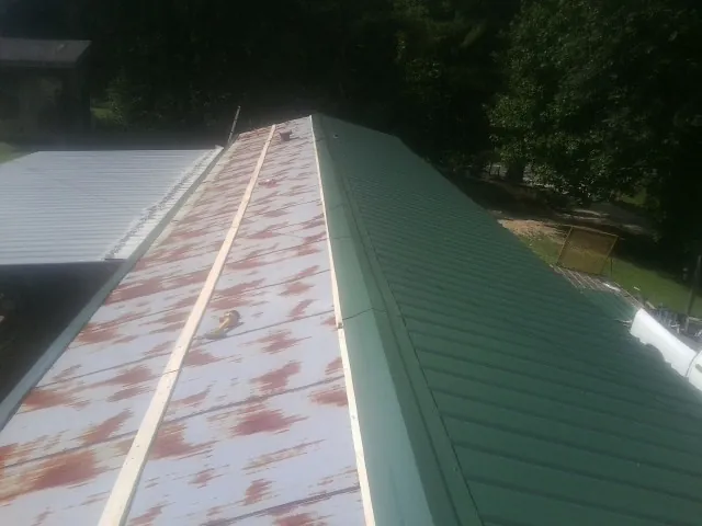 Old rusted panels beside newly installed green metal roofing — Wind Damage Roof Repair by Roofing Brothers in Langston