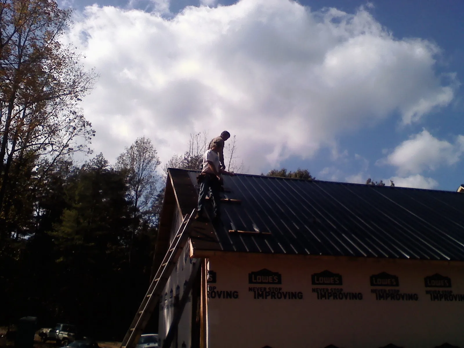 Roofer fastening dark metal panels high against a cloudy sky, from a Roof Inspection job in Langston