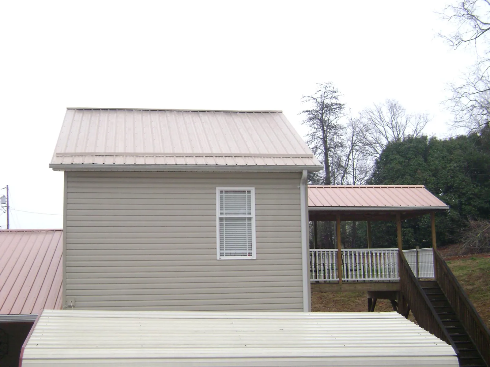 Tan metal roofs on a two story addition and attached porch, from a Roof Replacement job in Langston